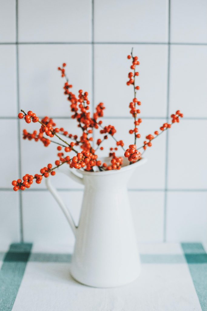 Bright red winter berries elegantly arranged in a white vase against a minimalist tiled background.